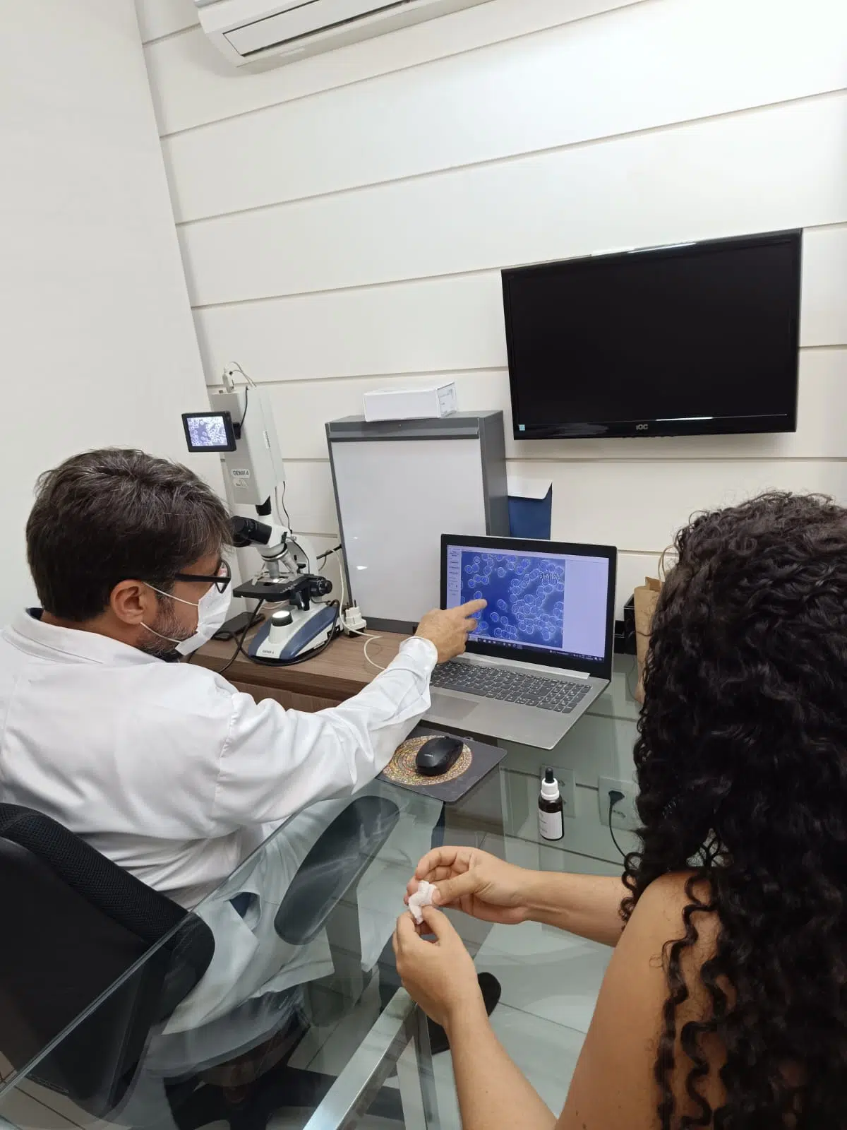 Dr. Marcelo Chiarini apontando para a tela do microscópio durante análise de sangue vivo com paciente — investigação do bioterreno no tratamento da ATM em Salvador