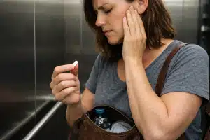 Mulher sentindo dor na região da mandíbula enquanto segura analgésico, representando dor de cabeça persistente com exame normal em Salvador